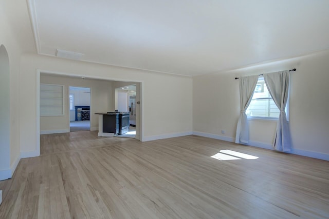 unfurnished room featuring light wood finished floors, baseboards, built in features, a fireplace, and arched walkways