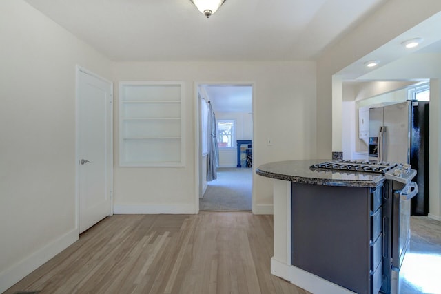 kitchen featuring dark stone countertops, built in shelves, baseboards, stainless steel gas stove, and a center island