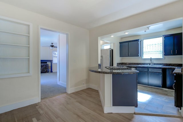 kitchen featuring light wood-style flooring, a sink, appliances with stainless steel finishes, a peninsula, and baseboards