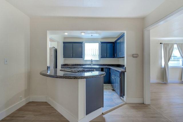 kitchen featuring a peninsula, blue cabinets, plenty of natural light, and light wood finished floors