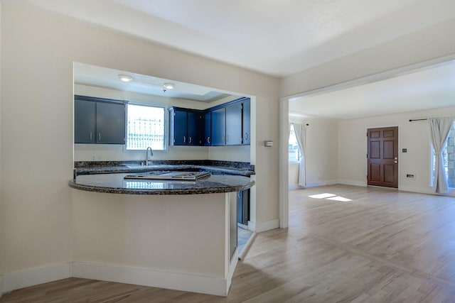 kitchen with baseboards, a peninsula, a sink, light wood-style floors, and blue cabinets