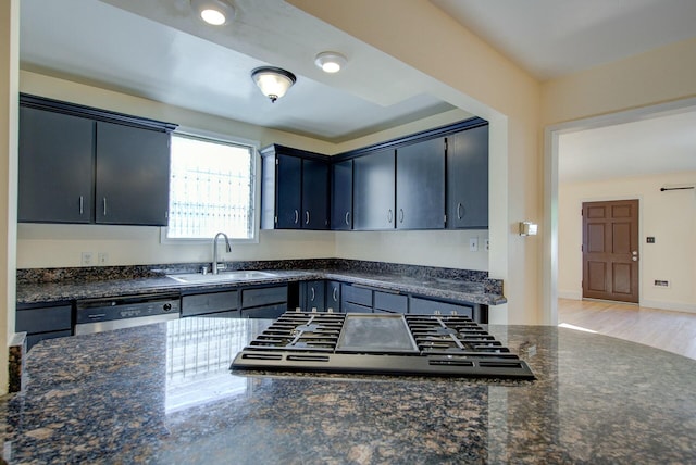 kitchen with light wood-style flooring, a sink, dark stone countertops, stainless steel dishwasher, and cooktop