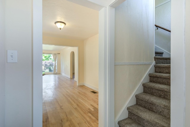 staircase with visible vents, arched walkways, baseboards, and wood finished floors