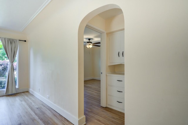 hall featuring ornamental molding, light wood-style floors, arched walkways, and baseboards