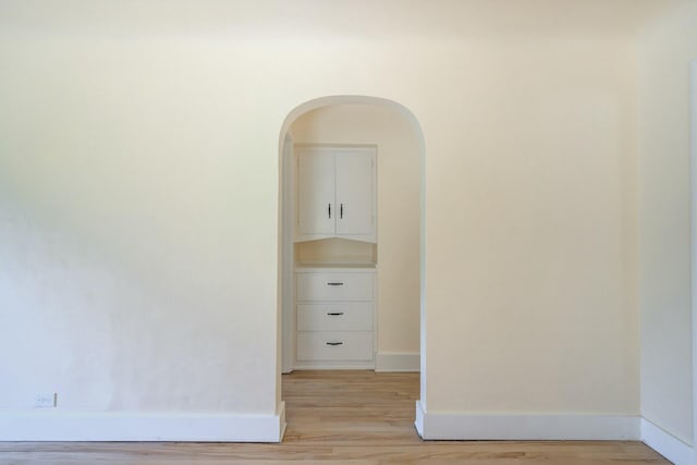 spare room featuring baseboards, light wood-type flooring, and arched walkways