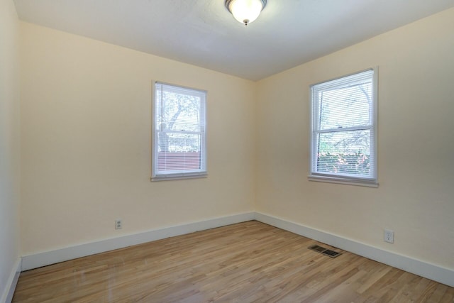 unfurnished room with a wealth of natural light, visible vents, baseboards, and light wood-style floors