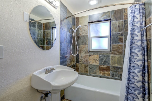 bathroom with a sink, shower / tub combo with curtain, and a textured wall