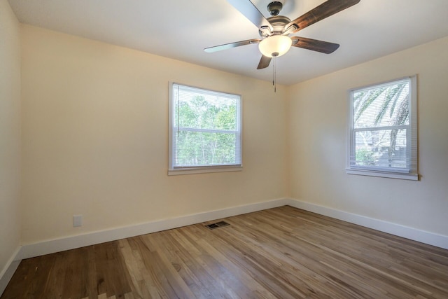 spare room with ceiling fan, visible vents, baseboards, and wood finished floors