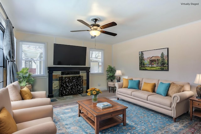 living room with a wealth of natural light, a tiled fireplace, ceiling fan, and ornamental molding