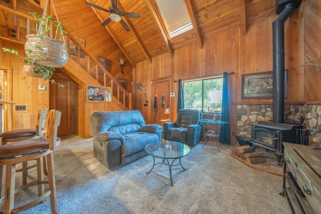 living area featuring wooden walls, carpet floors, wood ceiling, beam ceiling, and a wood stove