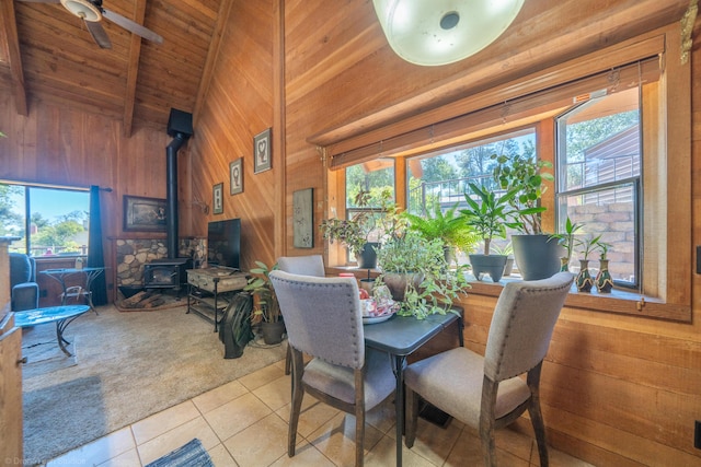 carpeted dining area with wooden ceiling, a wood stove, wood walls, high vaulted ceiling, and beam ceiling