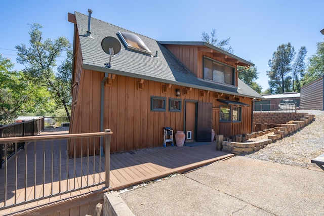 view of front facade with a shingled roof, board and batten siding, and a wooden deck