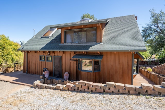 view of front facade featuring a deck, a shingled roof, board and batten siding, and fence