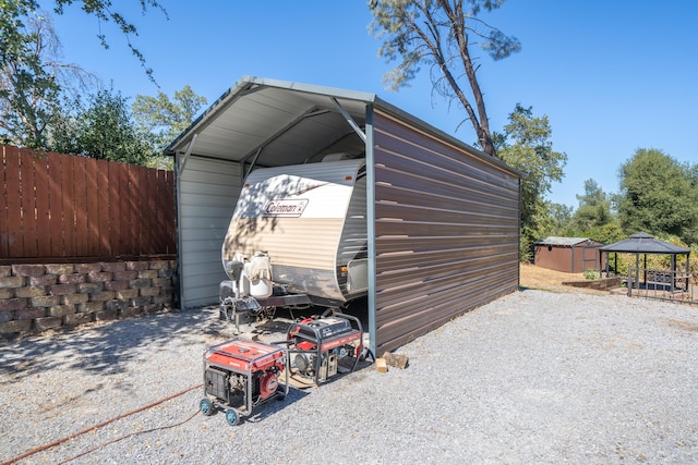 view of shed with a detached carport, gravel driveway, and fence