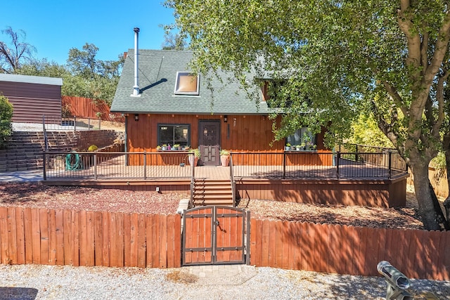 chalet / cabin featuring a fenced front yard, a gate, a shingled roof, and a deck