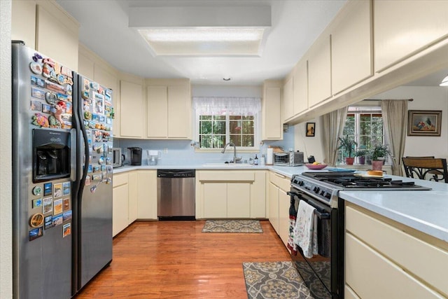 kitchen with light countertops, stainless steel appliances, a sink, light wood-style floors, and cream cabinets