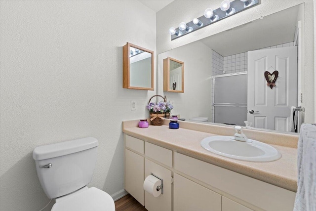 full bathroom with a textured wall, toilet, vanity, and a shower with shower door