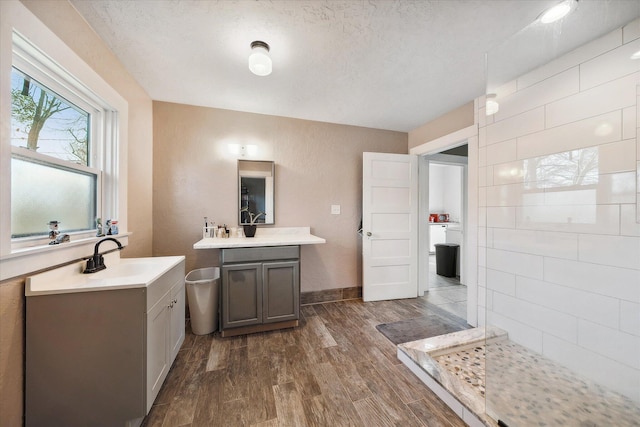 bathroom featuring a textured ceiling, wood finished floors, two vanities, a sink, and a tile shower