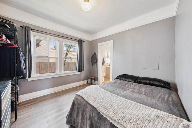 bedroom with ensuite bathroom, light wood-type flooring, and baseboards