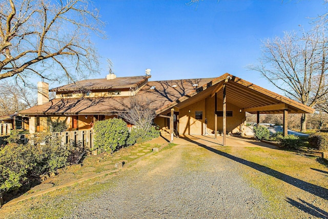 view of front of property featuring driveway, a chimney, a carport, and stucco siding