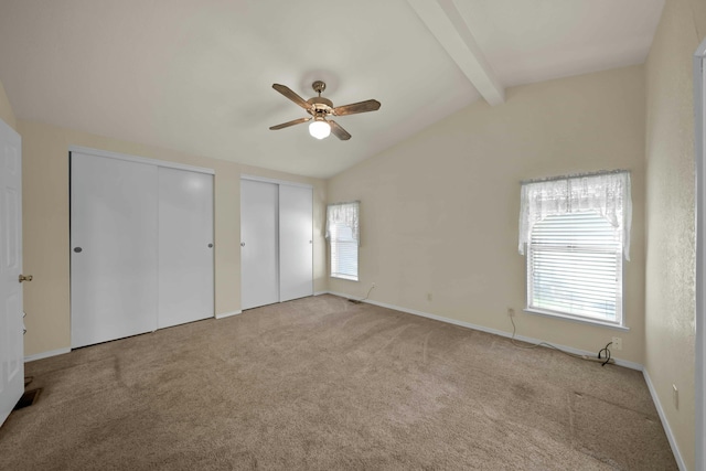 unfurnished bedroom featuring two closets, baseboards, carpet, lofted ceiling with beams, and a ceiling fan