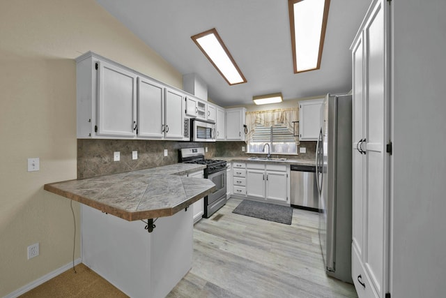 kitchen featuring a sink, backsplash, stainless steel appliances, a peninsula, and vaulted ceiling