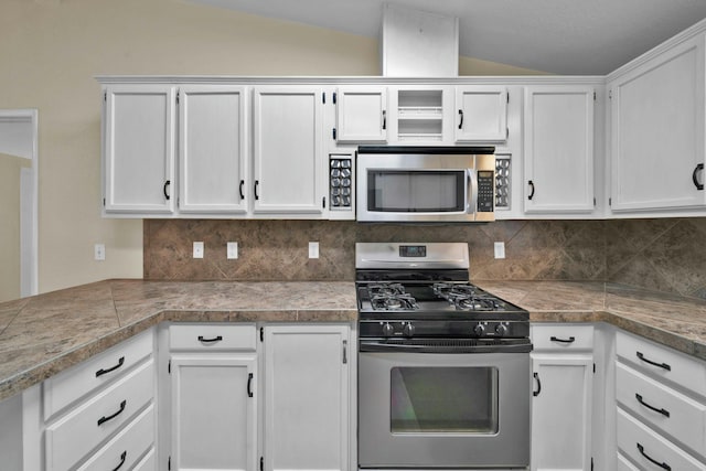 kitchen featuring tile countertops, lofted ceiling, decorative backsplash, appliances with stainless steel finishes, and white cabinets