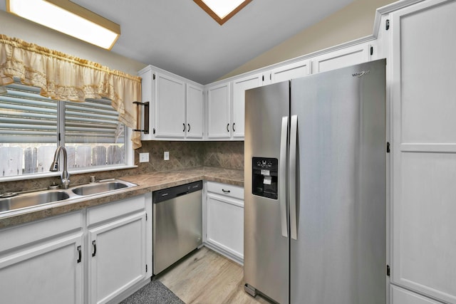 kitchen featuring a sink, white cabinetry, stainless steel appliances, light wood-style floors, and vaulted ceiling