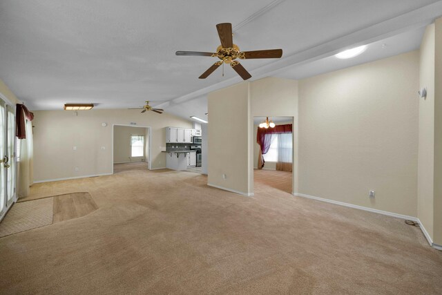 unfurnished living room with a healthy amount of sunlight, light colored carpet, a ceiling fan, and vaulted ceiling