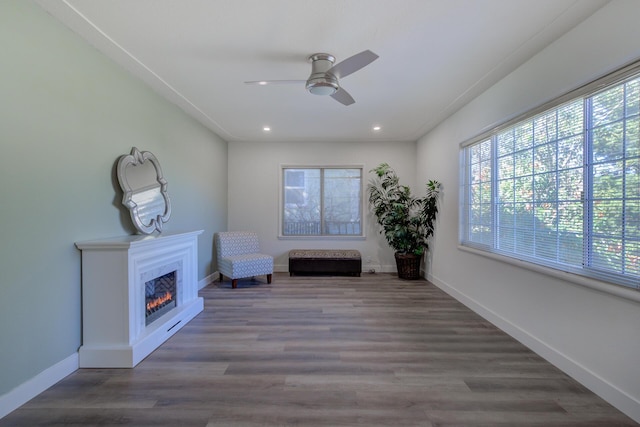 unfurnished room with a ceiling fan, wood finished floors, baseboards, recessed lighting, and a lit fireplace