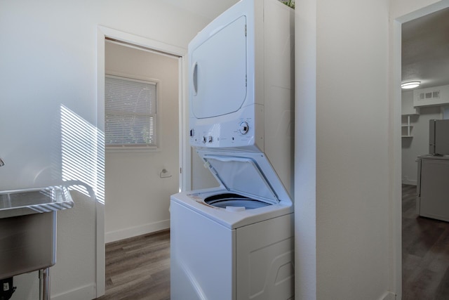 clothes washing area featuring laundry area, stacked washer and clothes dryer, baseboards, and wood finished floors