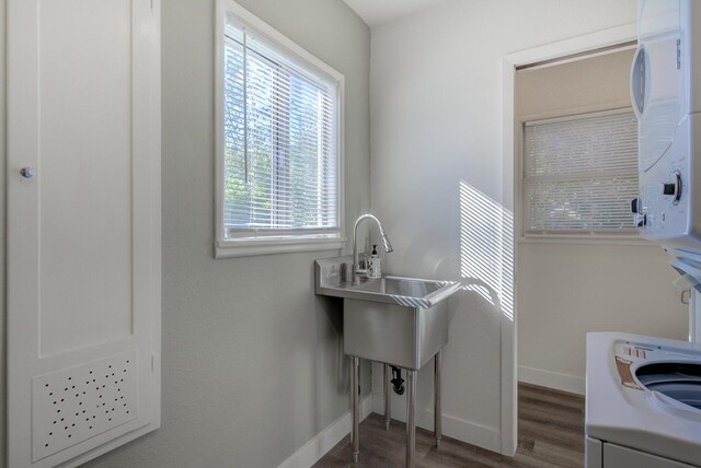 clothes washing area with baseboards, stacked washer and dryer, wood finished floors, and laundry area