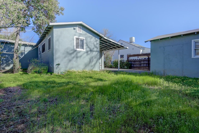 view of side of home with a carport, fence, and stucco siding