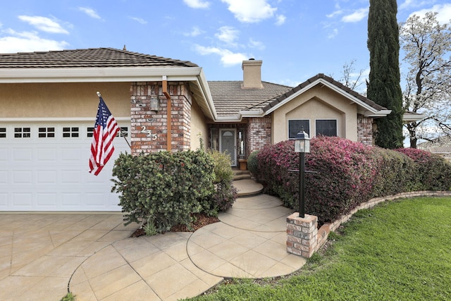 view of front facade with an attached garage, stucco siding, a chimney, a tiled roof, and brick siding