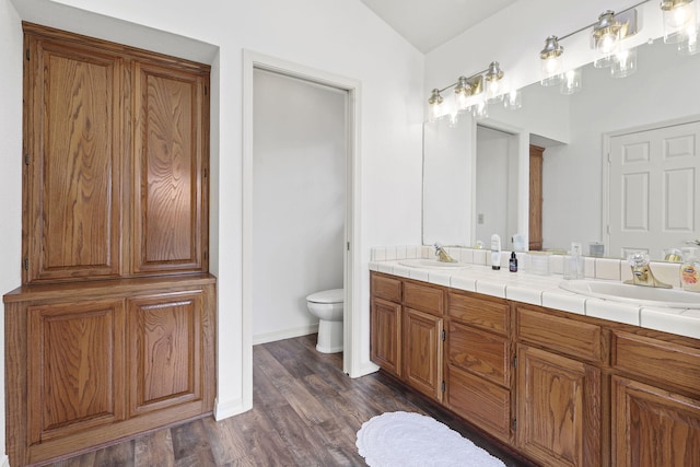 bathroom with a sink, toilet, wood finished floors, and double vanity