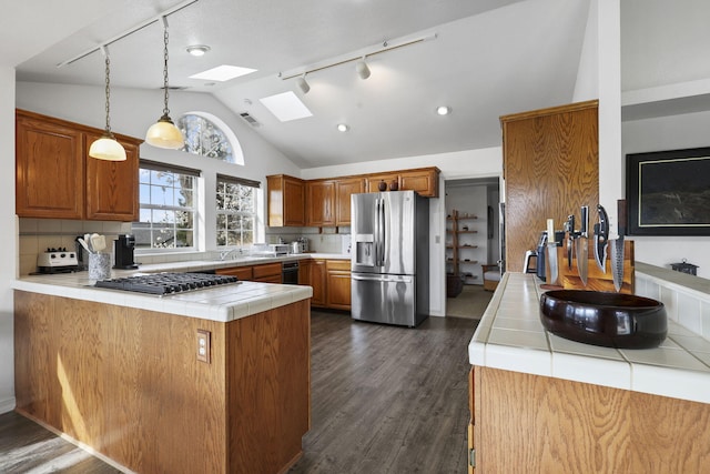 kitchen with tile countertops, a peninsula, vaulted ceiling with skylight, dark wood-style flooring, and appliances with stainless steel finishes