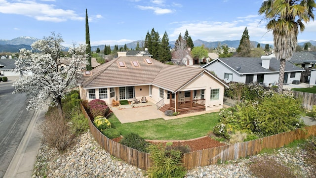 back of house featuring stucco siding, a fenced backyard, a yard, a mountain view, and a tiled roof