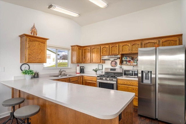 kitchen with a sink, under cabinet range hood, stainless steel appliances, a peninsula, and light countertops