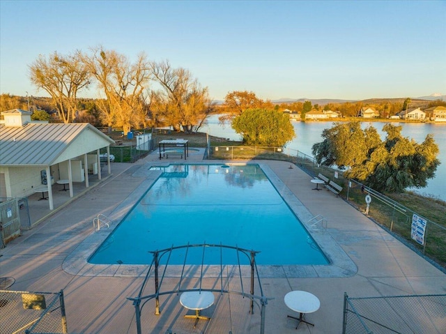 pool featuring a patio, fence, and a water view