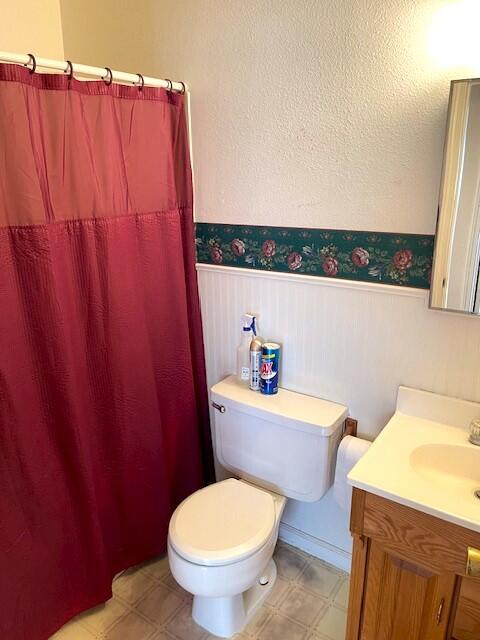 bathroom with tile patterned floors, a wainscoted wall, toilet, curtained shower, and vanity