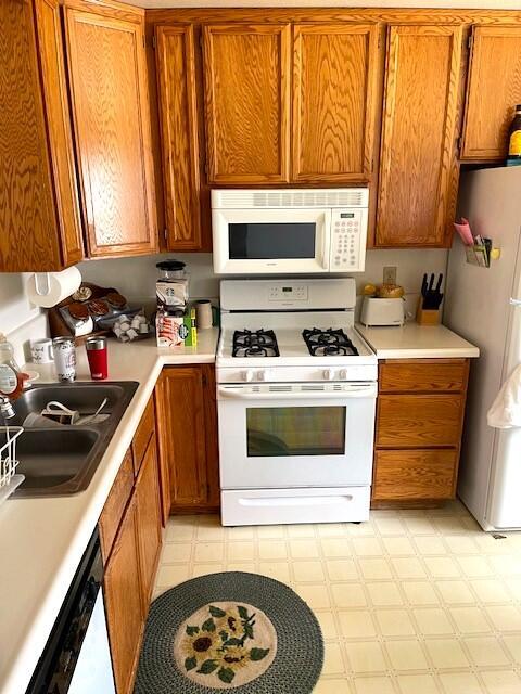 kitchen featuring brown cabinetry, light floors, white appliances, and a sink