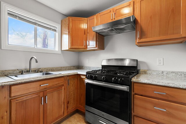 kitchen with a sink, under cabinet range hood, stainless steel gas stove, and brown cabinets