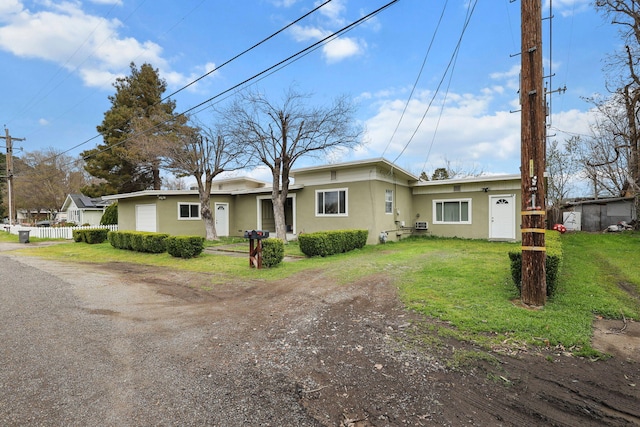 ranch-style home with fence, dirt driveway, a garage, a front lawn, and stucco siding