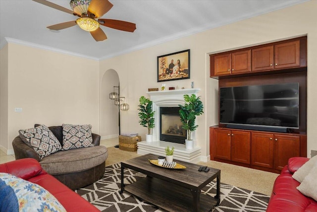 carpeted living area featuring a fireplace with raised hearth, crown molding, baseboards, ceiling fan, and arched walkways