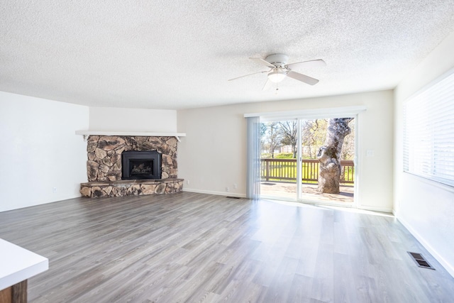 unfurnished living room with visible vents, ceiling fan, a stone fireplace, wood finished floors, and a textured ceiling