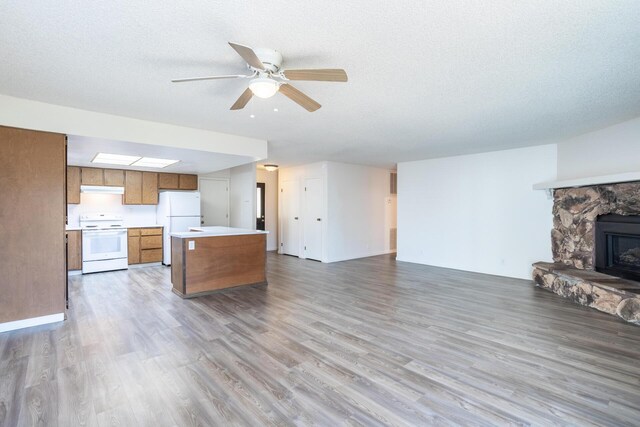 kitchen featuring brown cabinets, under cabinet range hood, open floor plan, white appliances, and light countertops