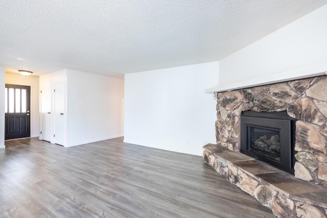 living room featuring a textured ceiling, a stone fireplace, and wood finished floors