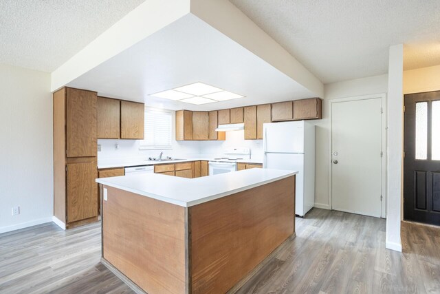 kitchen featuring white appliances, baseboards, light wood-style flooring, a sink, and under cabinet range hood