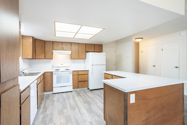 kitchen with under cabinet range hood, light wood-style floors, brown cabinetry, white appliances, and a sink