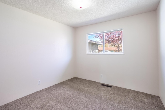 carpeted spare room with visible vents and a textured ceiling